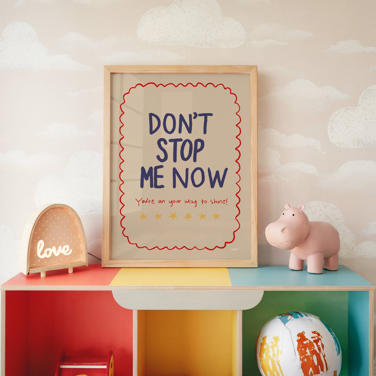 Dont stop me now star lettering nursery print in an oak frame on a rainbow toy shelf against cloud wallpaper