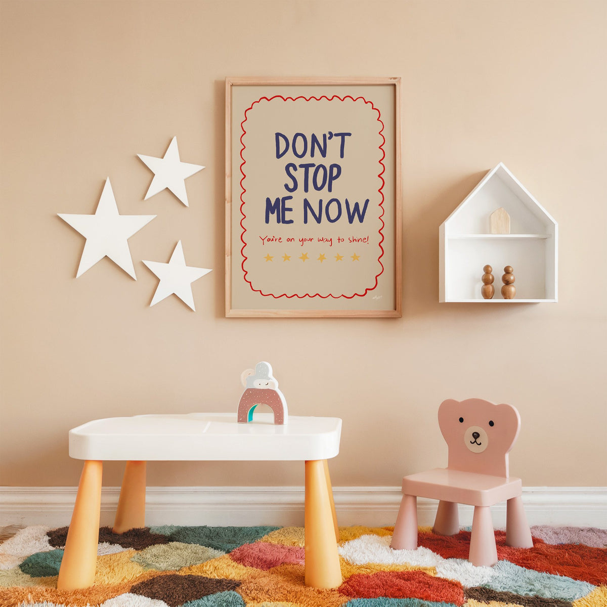 Dont stop me now star lettering nursery print in an oak frame on a peach wall above a kids table with wall stars