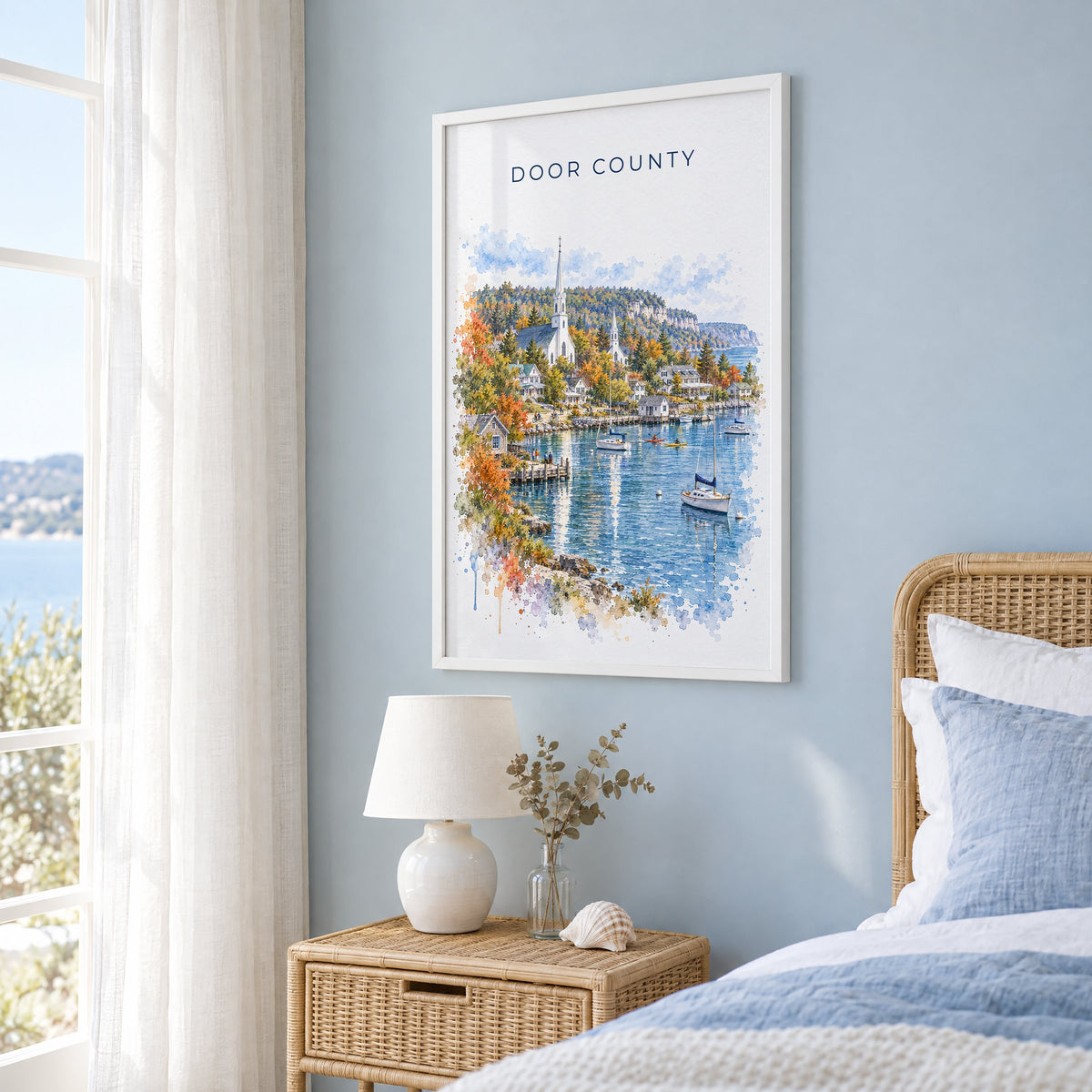 Door County watercolor print in a white frame on a pale blue wall beside a rattan bed in a coastal bedroom
