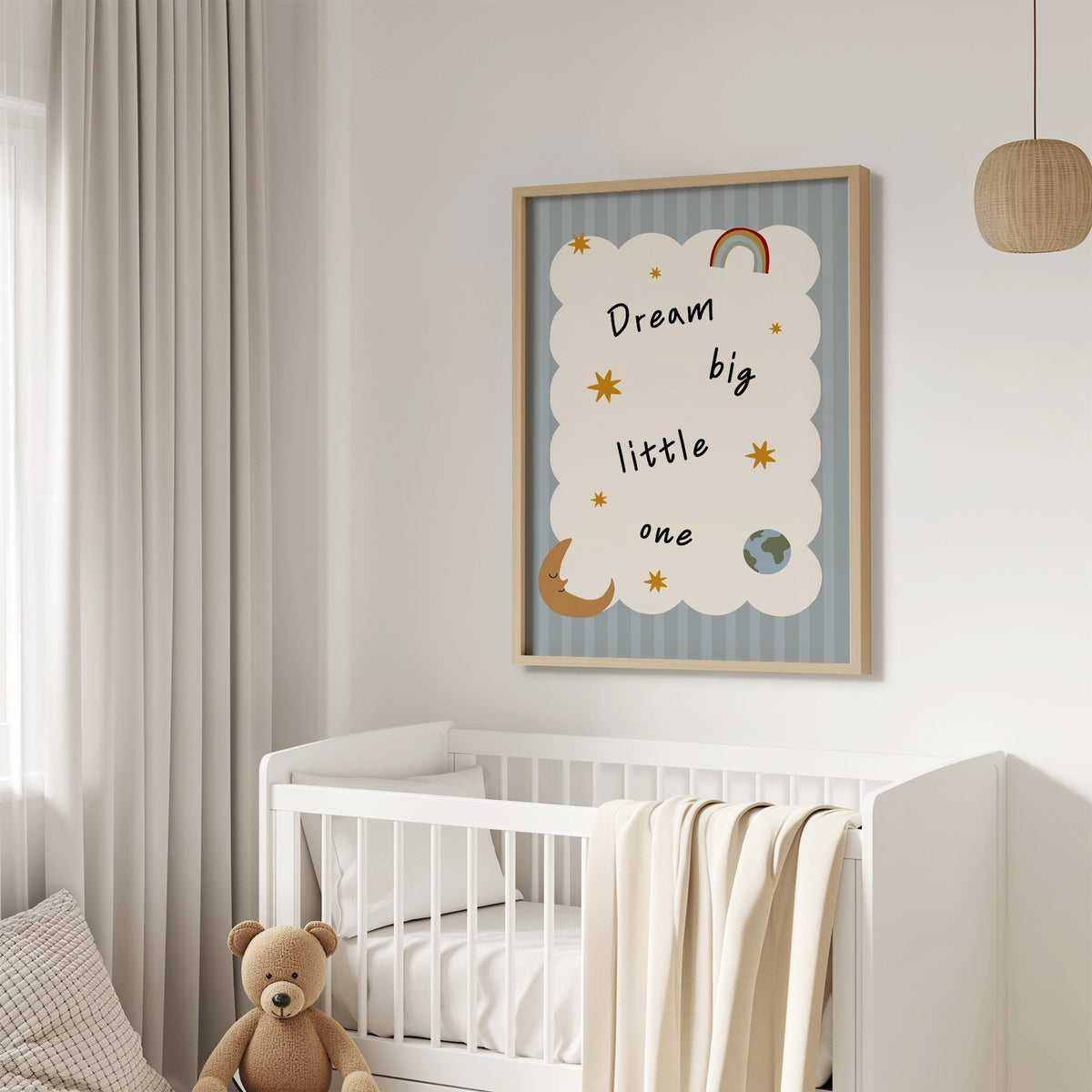 Dream big little one rainbow nursery print in an oak frame above a white crib with a teddy bear