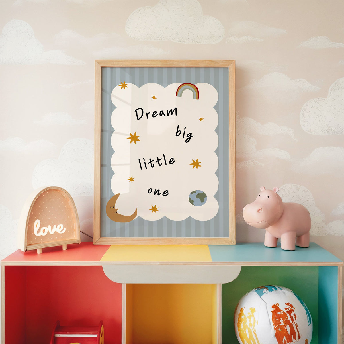Dream big little one rainbow nursery print in an oak frame on a rainbow toy shelf against cloud wallpaper