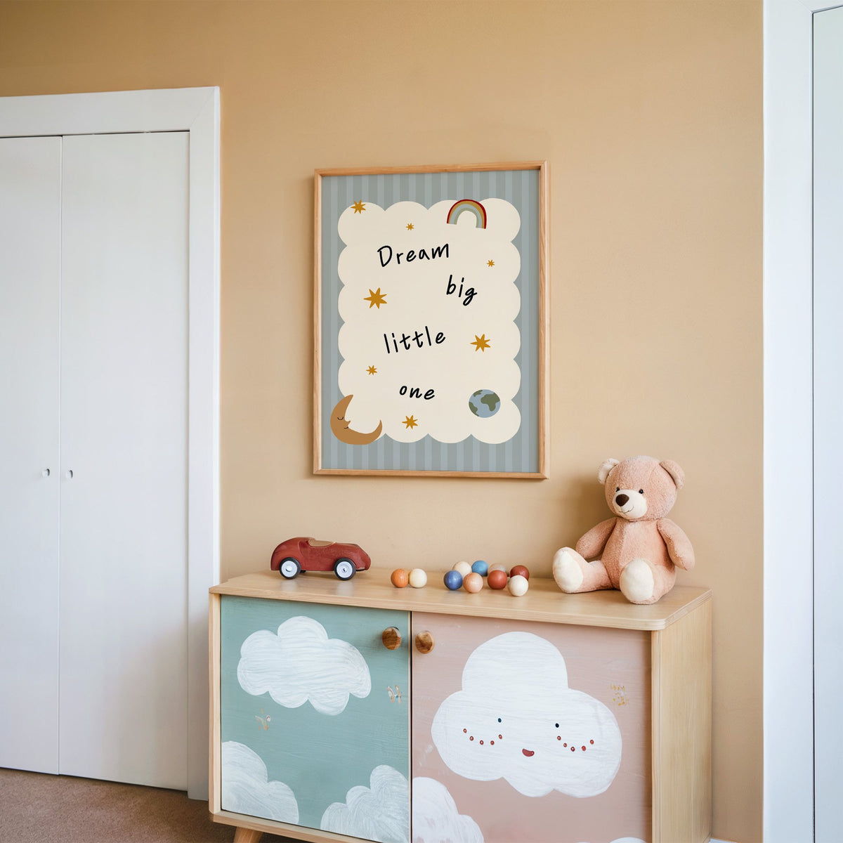 Dream big little one rainbow nursery print in an oak frame on a peach wall above a cloud-painted cabinet