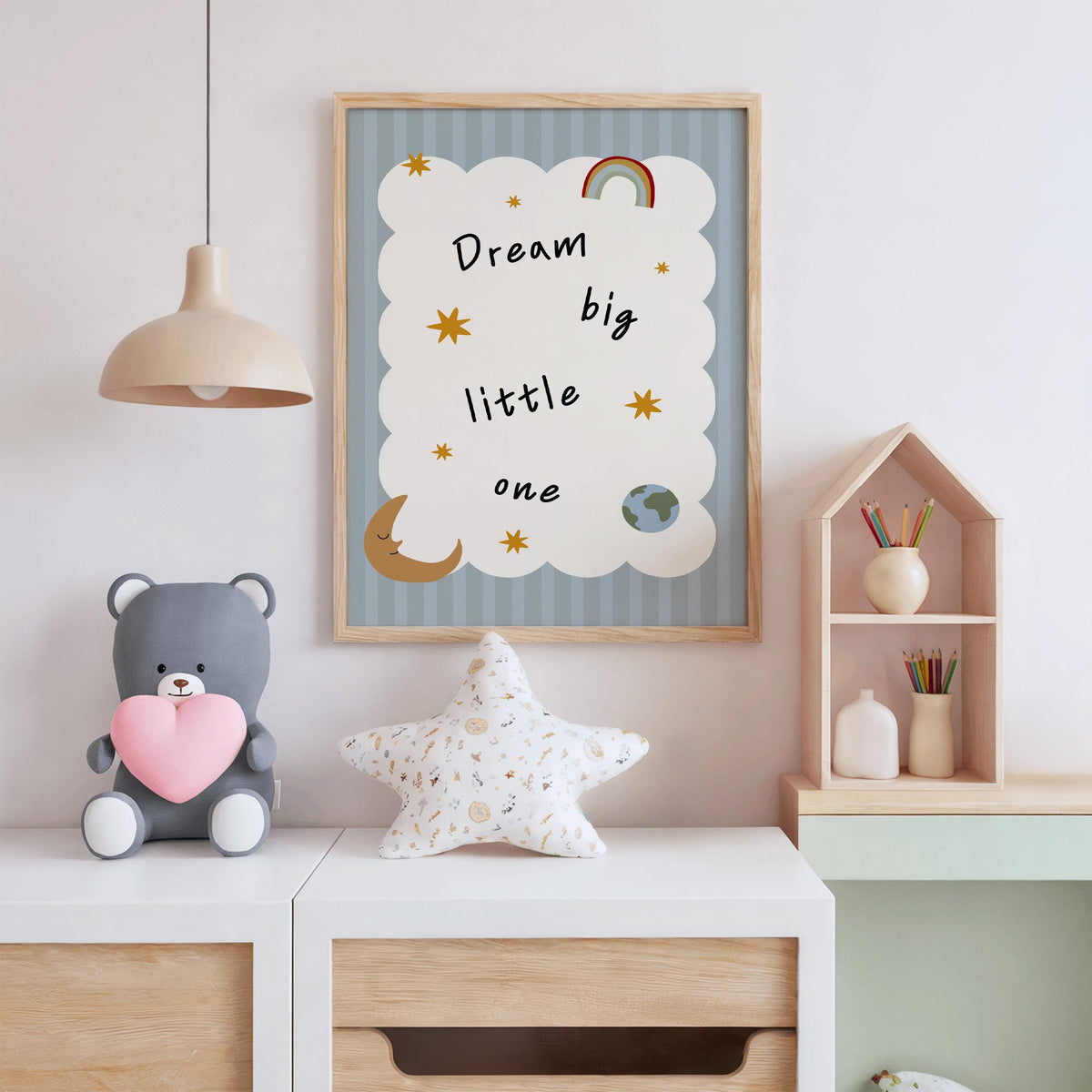 Dream big little one rainbow nursery print in an oak frame above a white dresser with a star pillow and house shelf