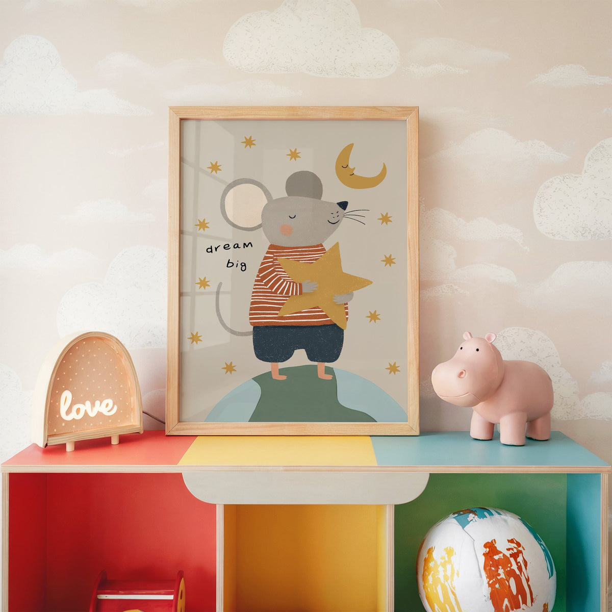 Dream big mouse hugging star nursery print in an oak frame on a rainbow toy shelf against cloud wallpaper