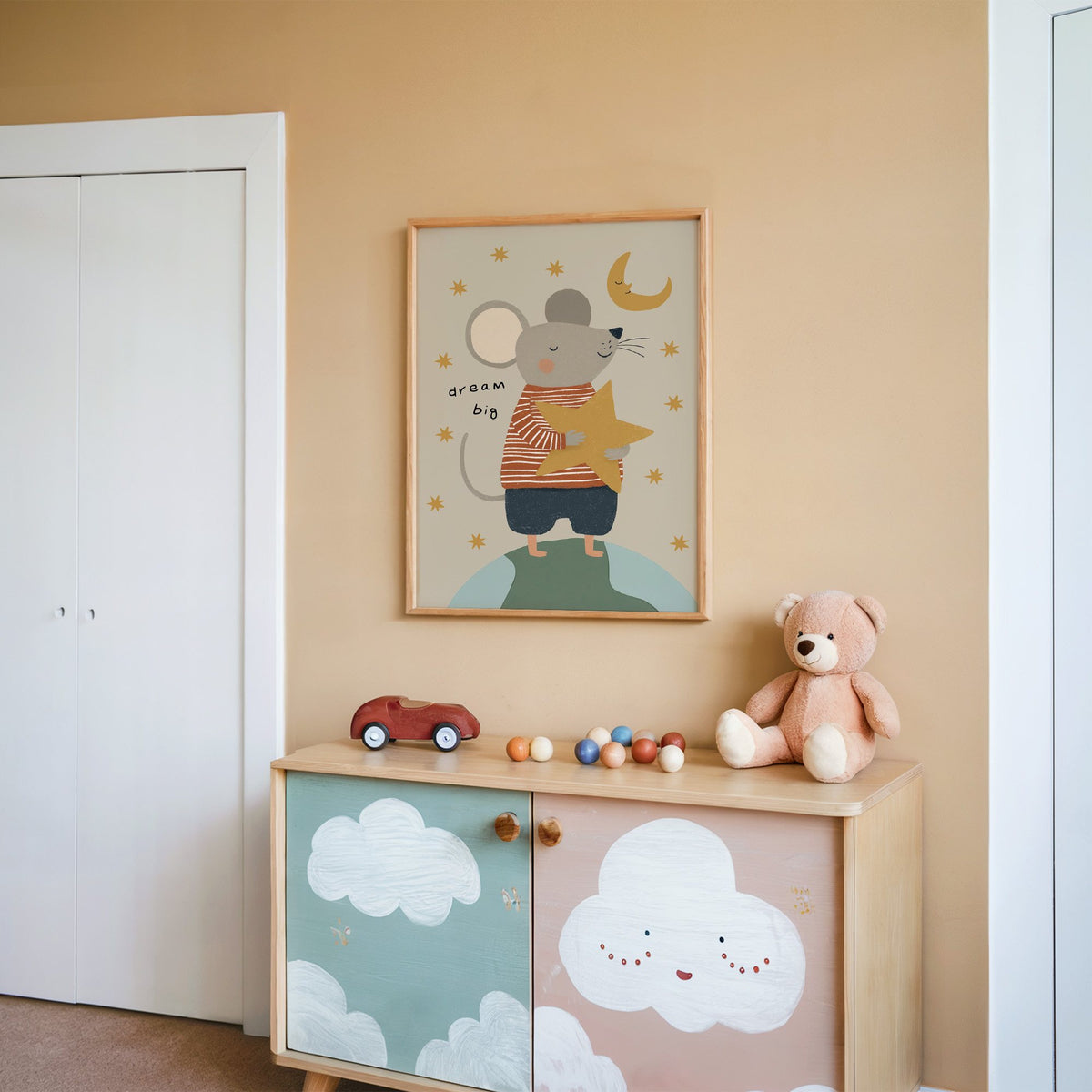 Dream big mouse hugging star nursery print in an oak frame on a peach wall above a cloud-painted cabinet