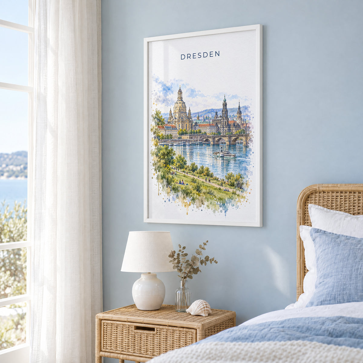 Dresden watercolor print in a white frame on a pale blue wall beside a rattan bed in a coastal bedroom