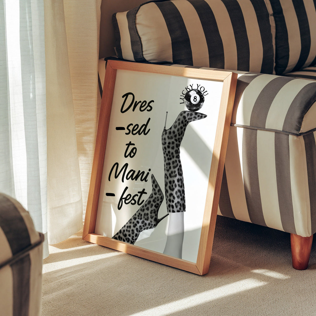 Legs in leopard boots balancing eight ball quote print in a pine frame leaning against a striped armchair