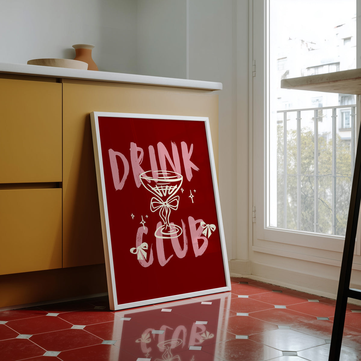 Drink Club print in a white frame against yellow cabinets on a red tiled floor