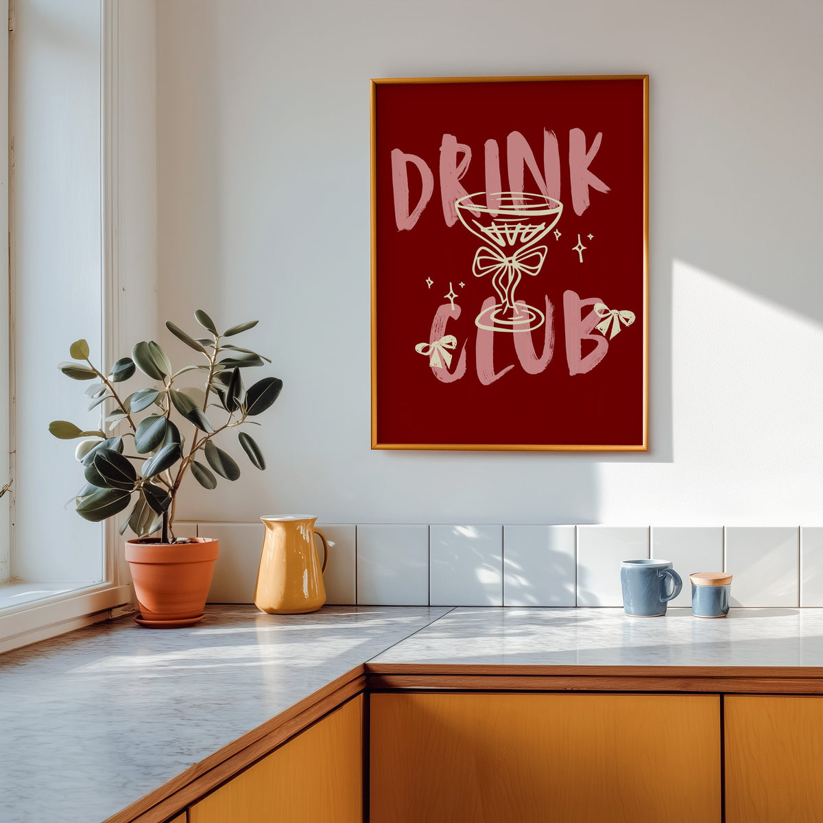 Drink Club print shown in a gold frame above a marble counter with a yellow ceramic jug