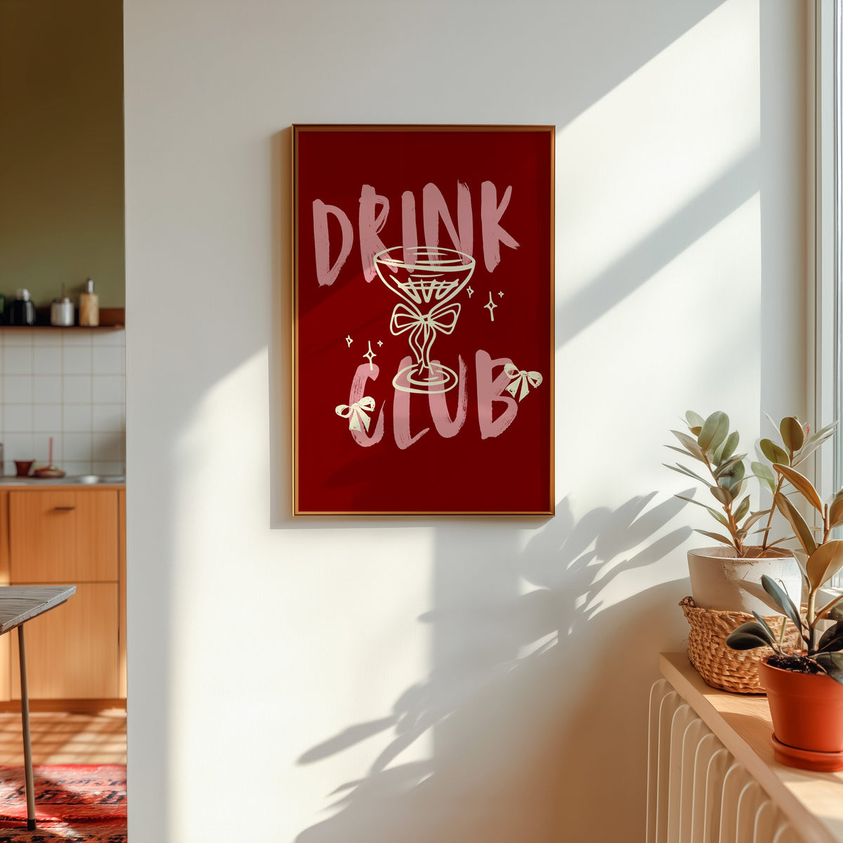 Drink Club print shown in a gold frame in sunlight with plants and a kitchen beyond
