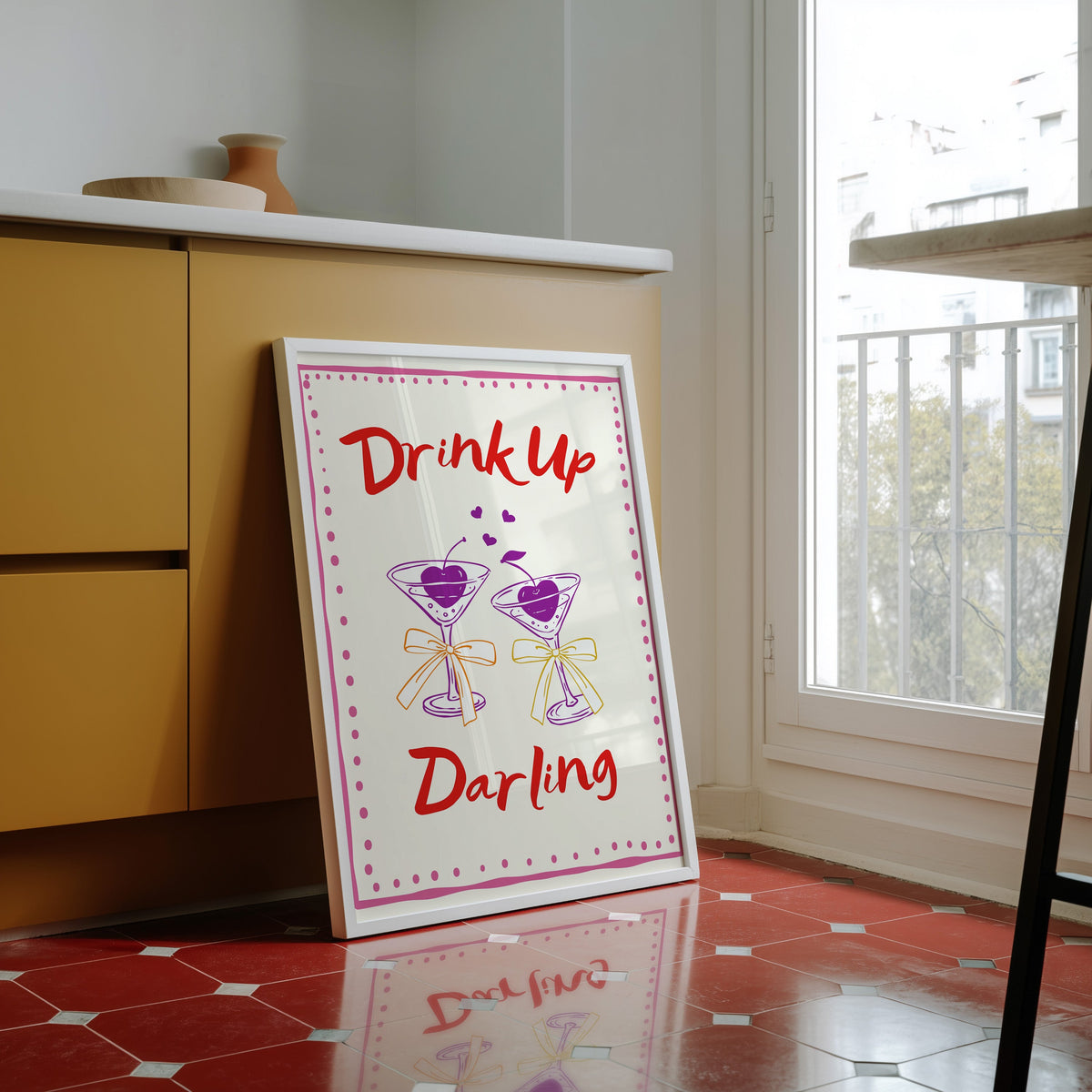 Drink Up Darling print in a white frame against yellow cabinets on a red tiled floor