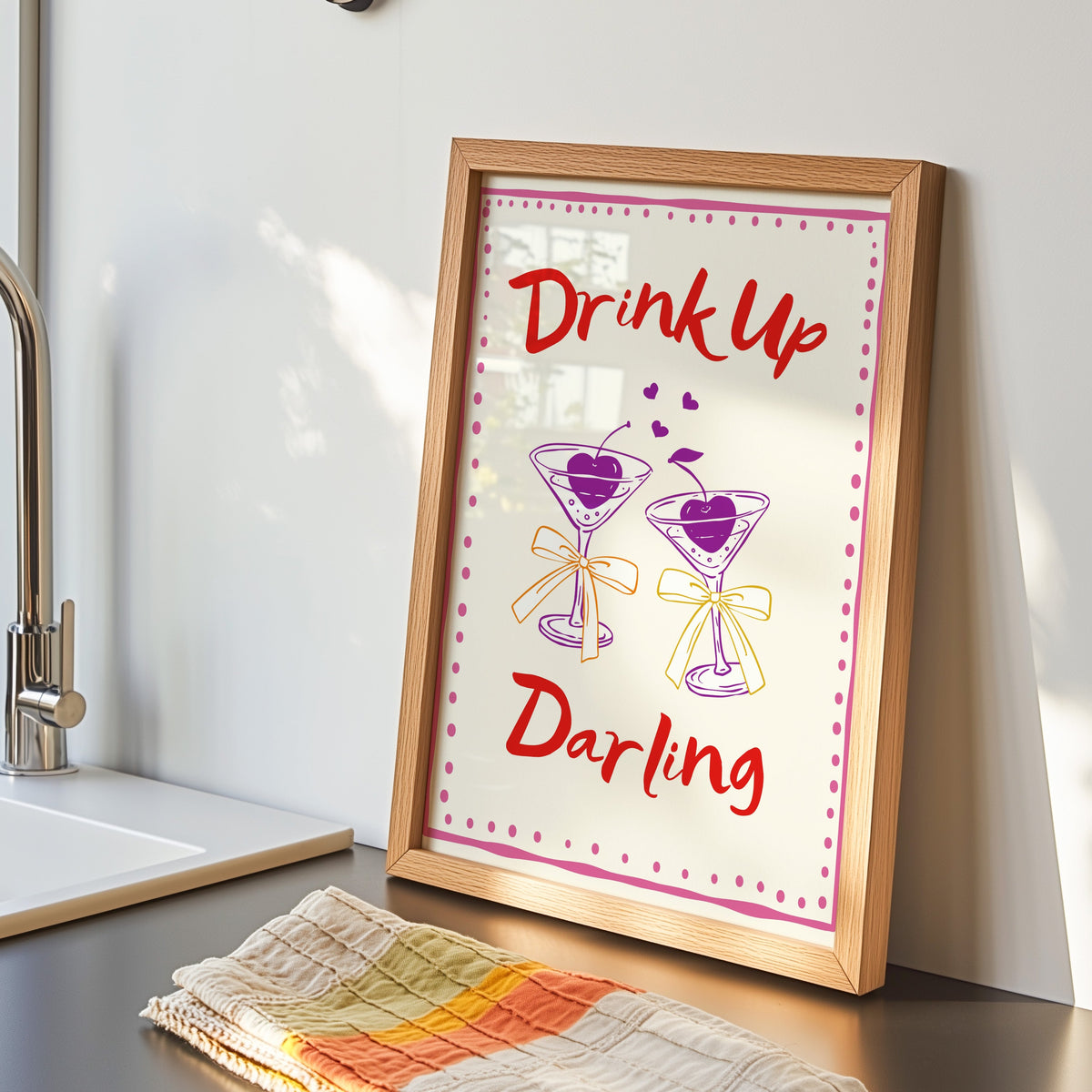 Drink Up Darling print in an oak frame by the kitchen sink beside a striped tea towel