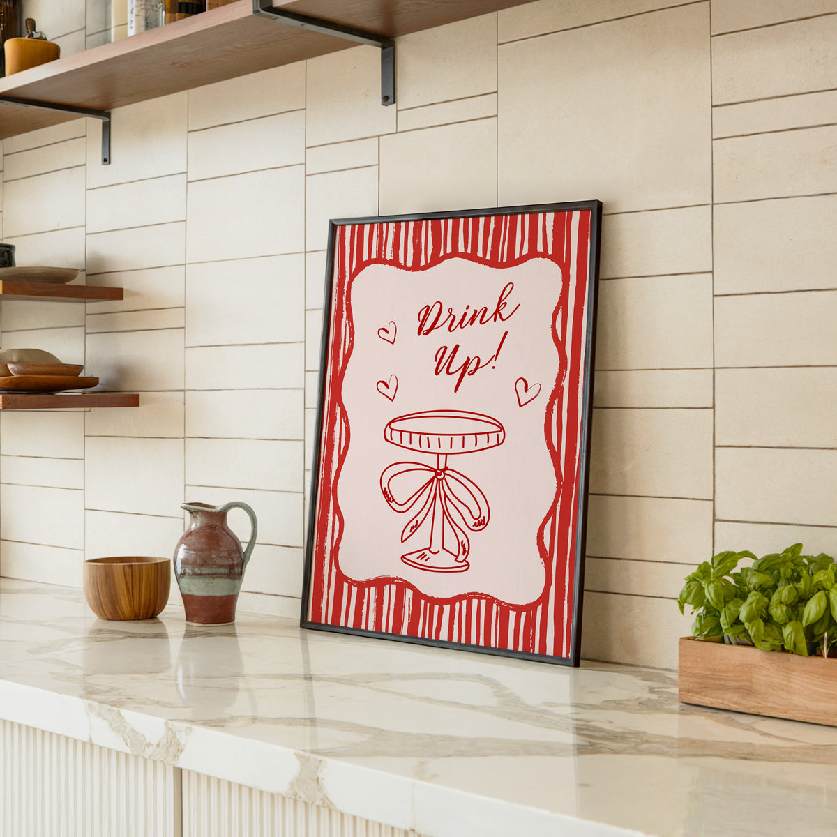 Drink Up coupe print in a black frame leaning on a marble counter in a tiled kitchen