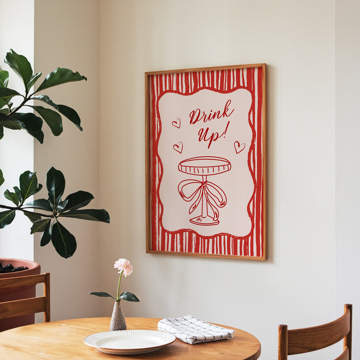Drink Up coupe print in a walnut frame above a round table beside a fiddle-leaf fig