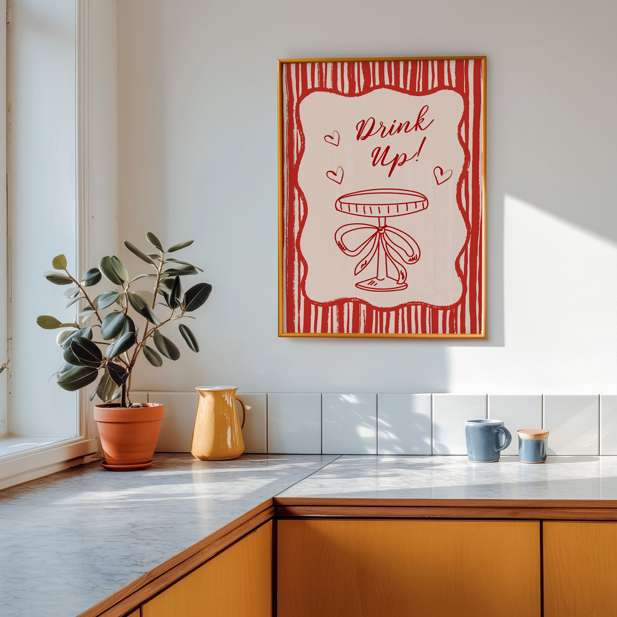 Drink Up coupe print shown in a gold frame above a marble counter in a tan kitchen