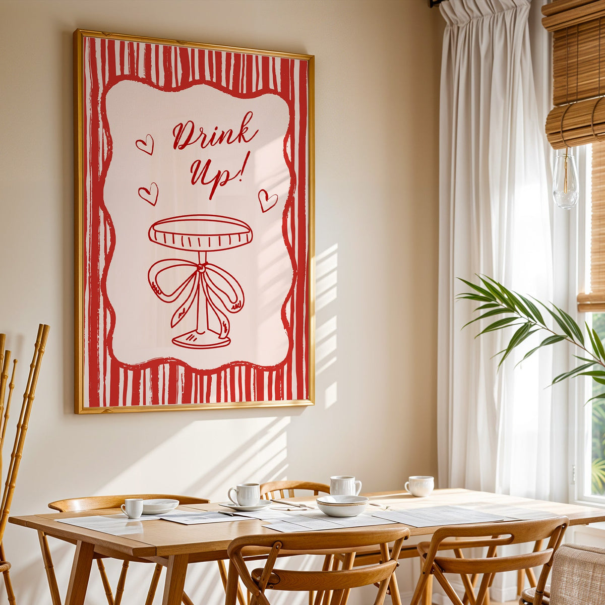 Drink Up coupe print shown in a gold frame above a breakfast table by a curtained window