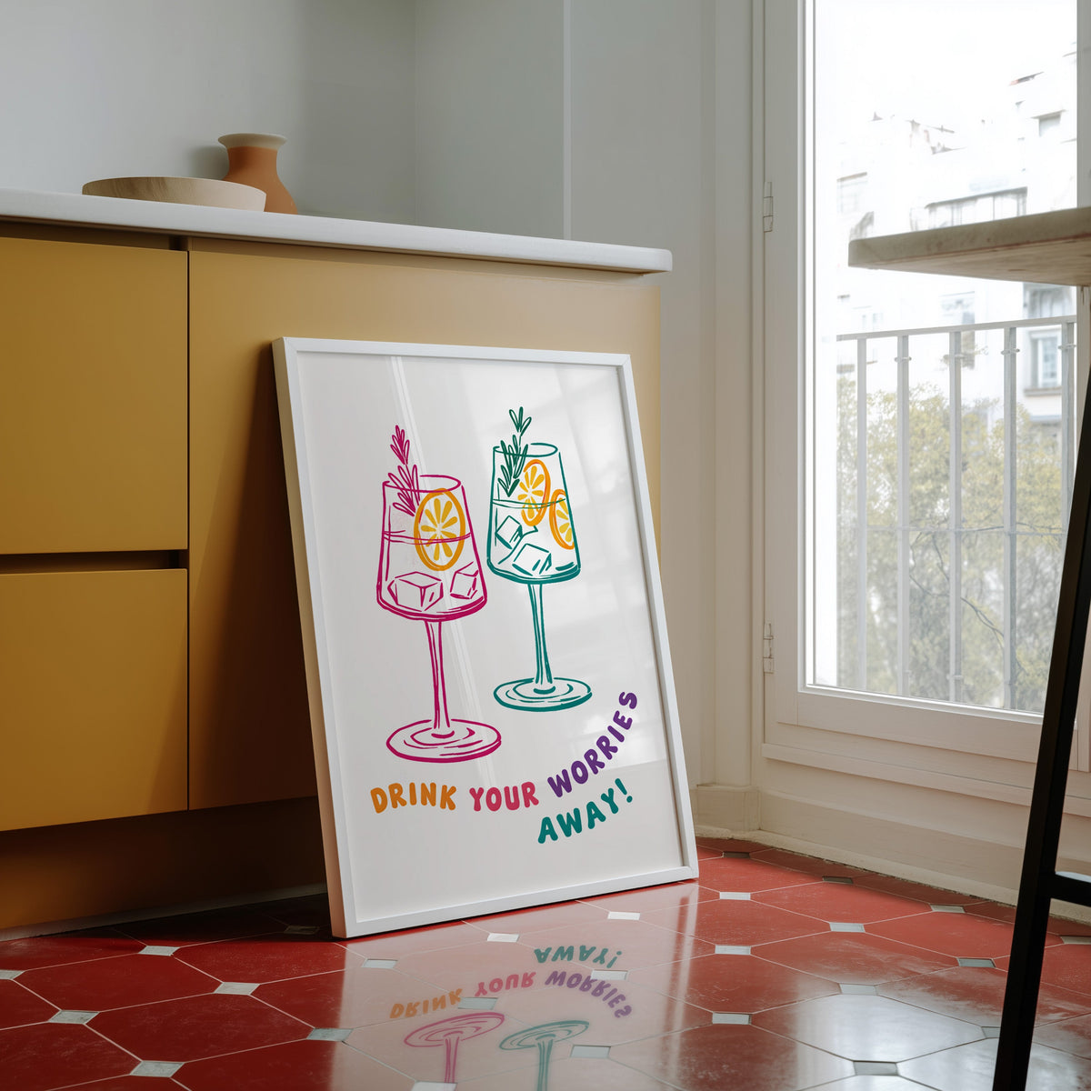 Drink Your Worries Away print in a white frame against yellow cabinets on a red tiled floor