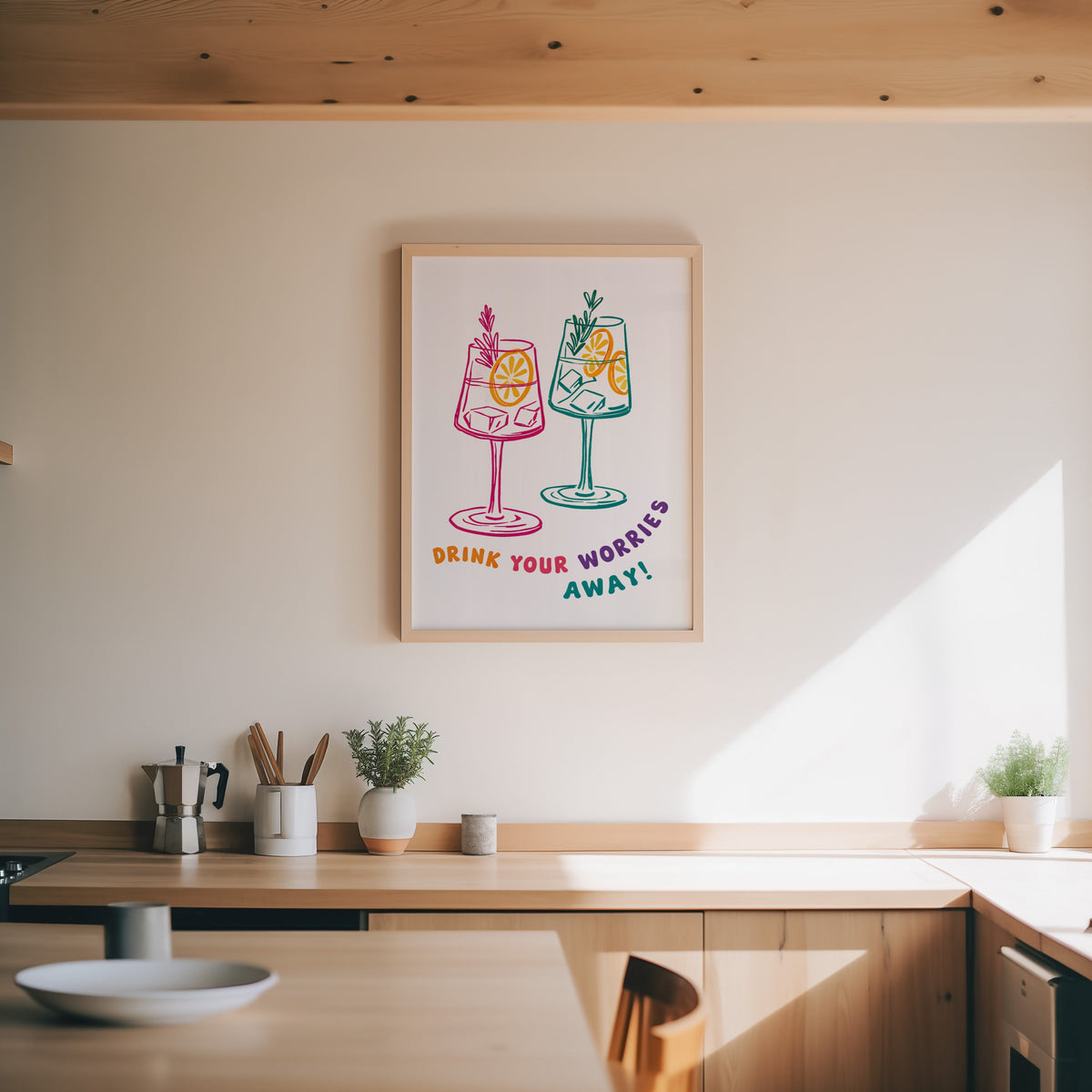 Drink Your Worries Away print in an oak frame above a wood counter with a moka pot and herbs