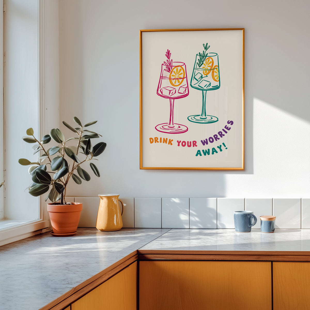 Drink Your Worries Away print shown in a gold frame above a marble counter with a yellow ceramic jug