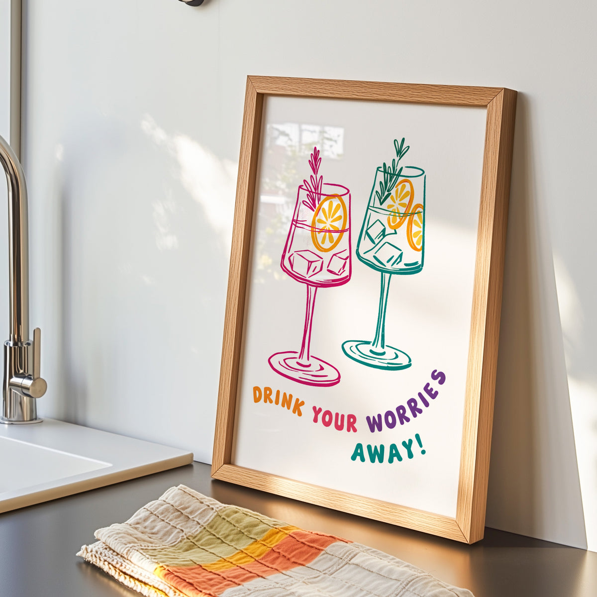 Drink Your Worries Away print in an oak frame by the kitchen sink beside a striped tea towel