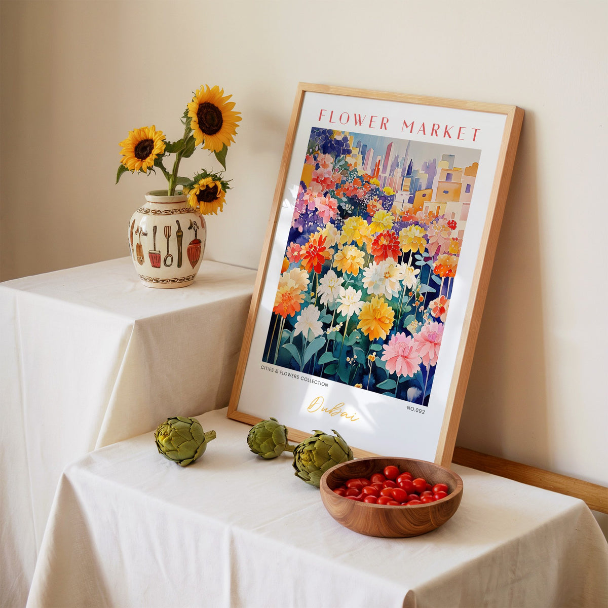 Dubai flower market print in an oak frame leaning on a linen-draped table beside a vase of sunflowers
