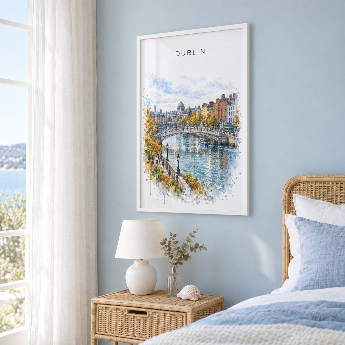 Dublin watercolor print in a white frame on a pale blue wall beside a rattan bed in a coastal bedroom