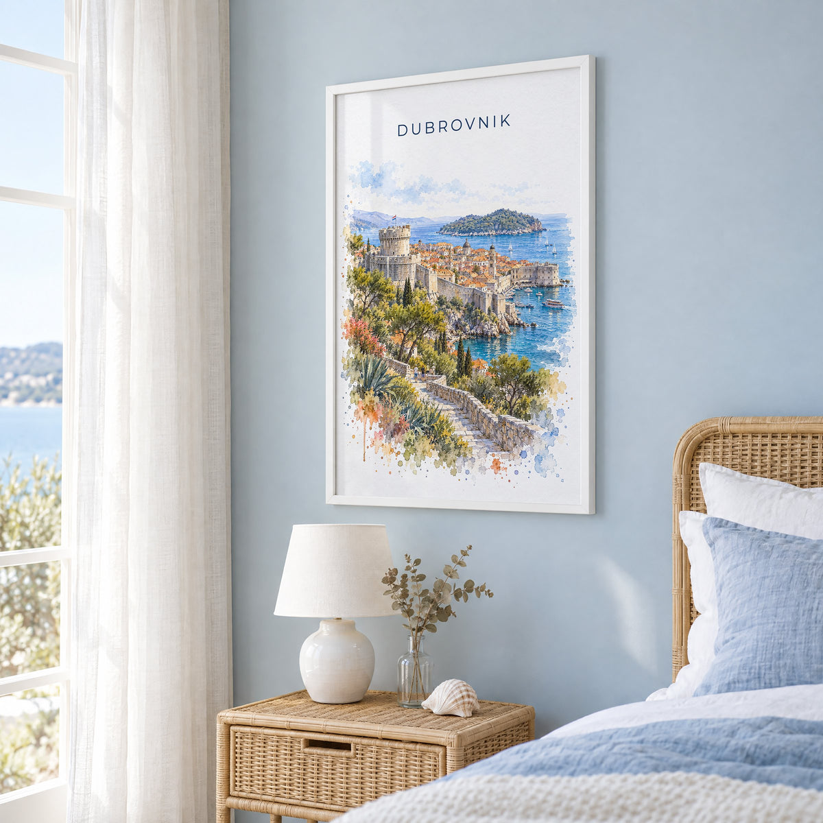Dubrovnik watercolor print in a white frame on a pale blue wall beside a rattan bed in a coastal bedroom
