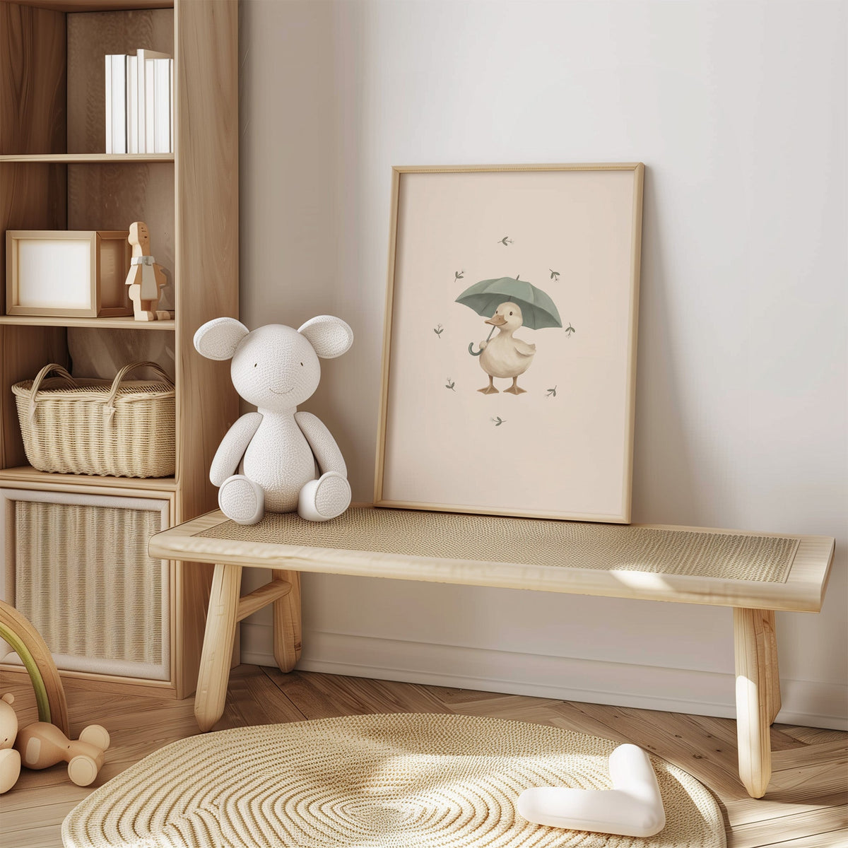 Cream duck holding a sage umbrella nursery print in an oak frame on a cane bench beside a white knit plush