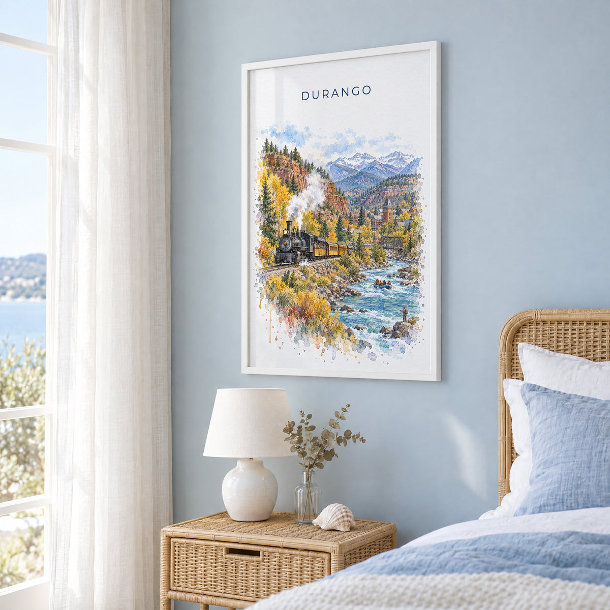 Durango, Colorado watercolor print in a white frame on a pale blue wall beside a rattan bed in a coastal bedroom