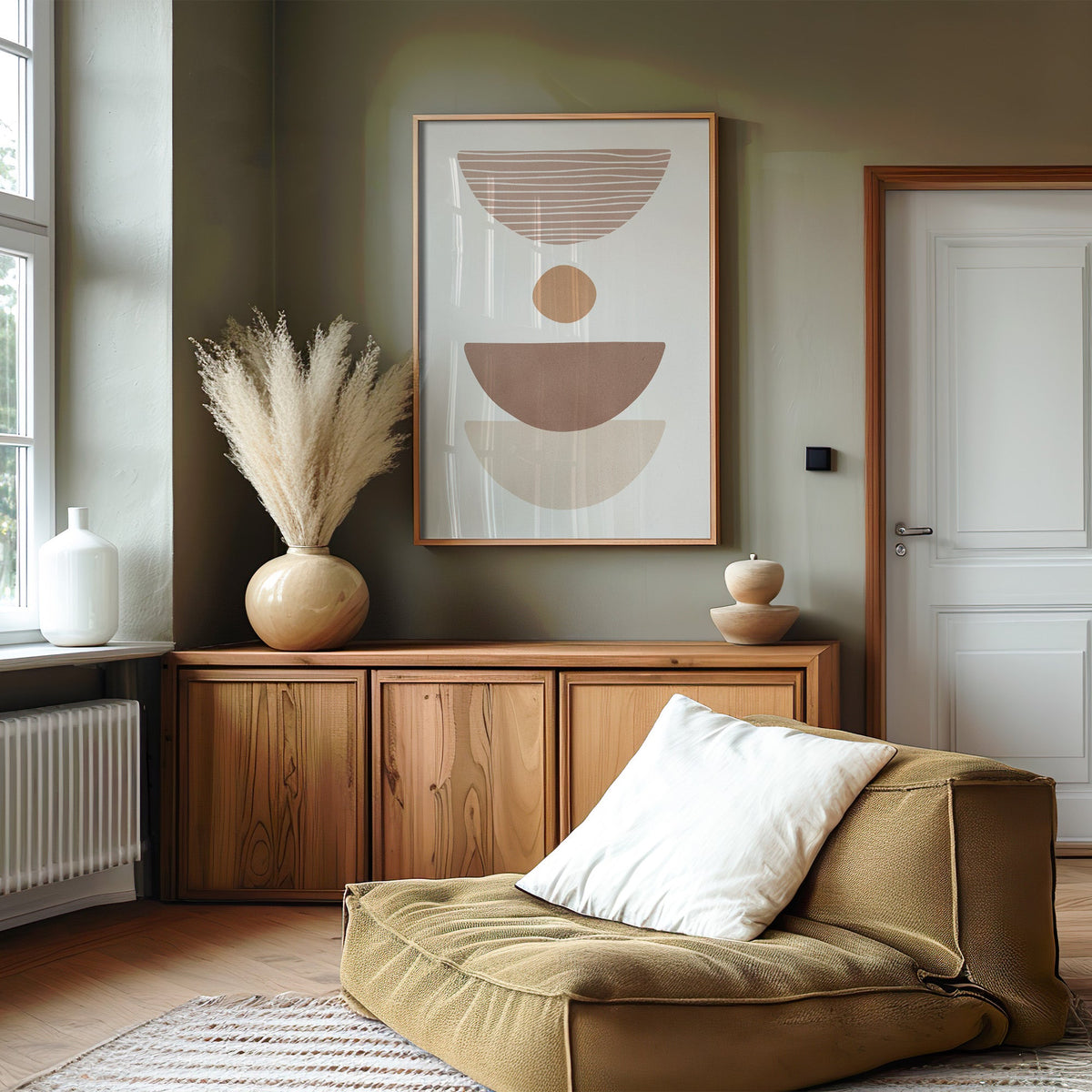 Dusty rose striped bowl shapes boho print in an oak frame on an olive green wall above a wood sideboard with pampas