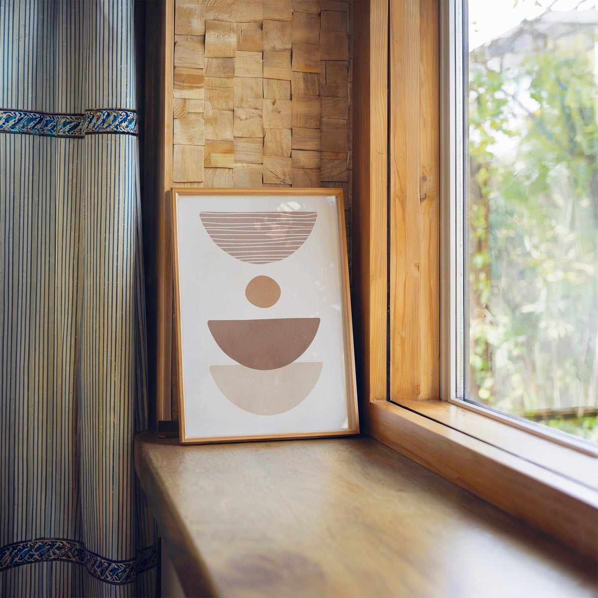 Dusty rose striped bowl shapes boho print in a light wood frame leaning on a wooden window sill by a garden view