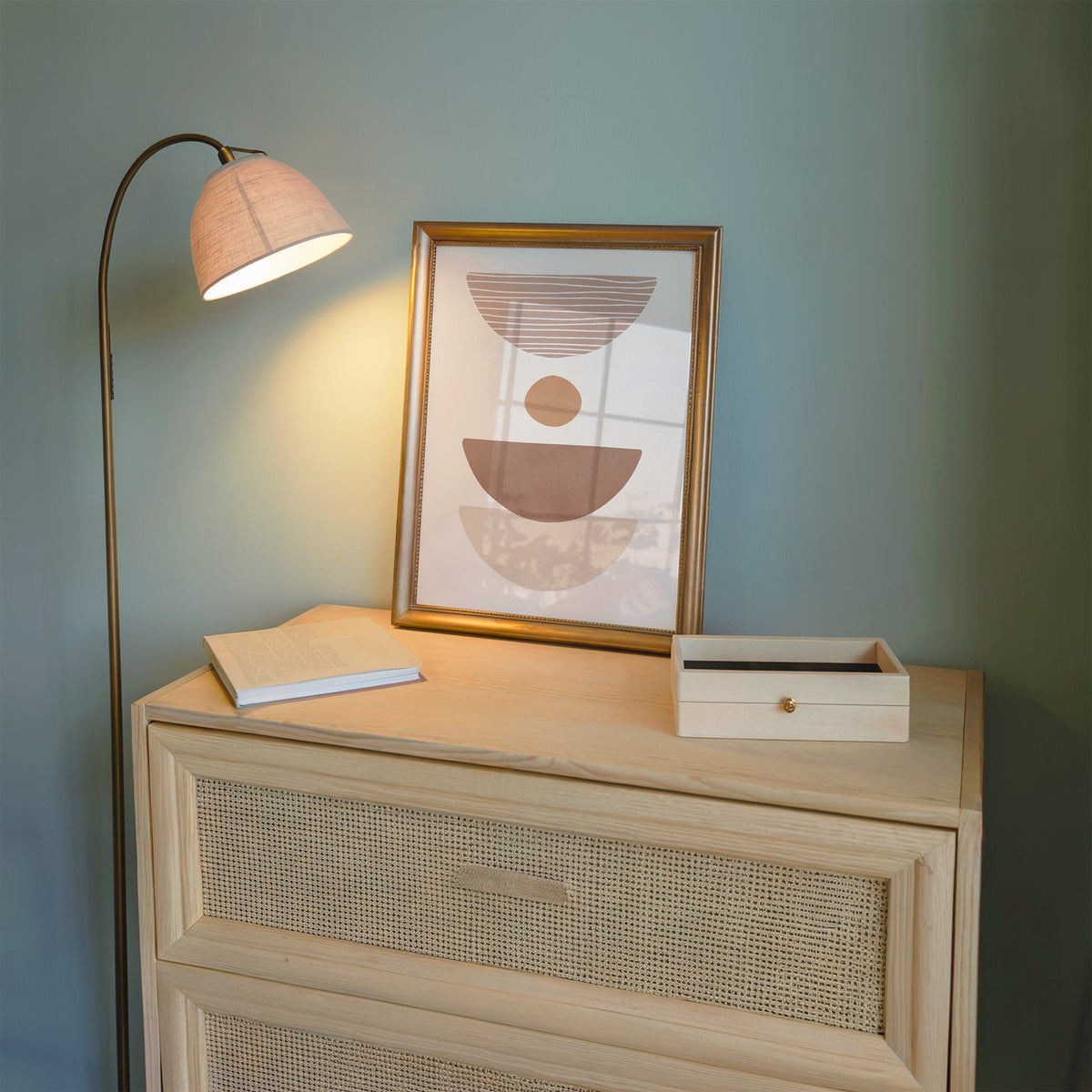 Dusty rose striped bowl shapes boho print shown in a gold frame on a cane dresser lit by a floor lamp