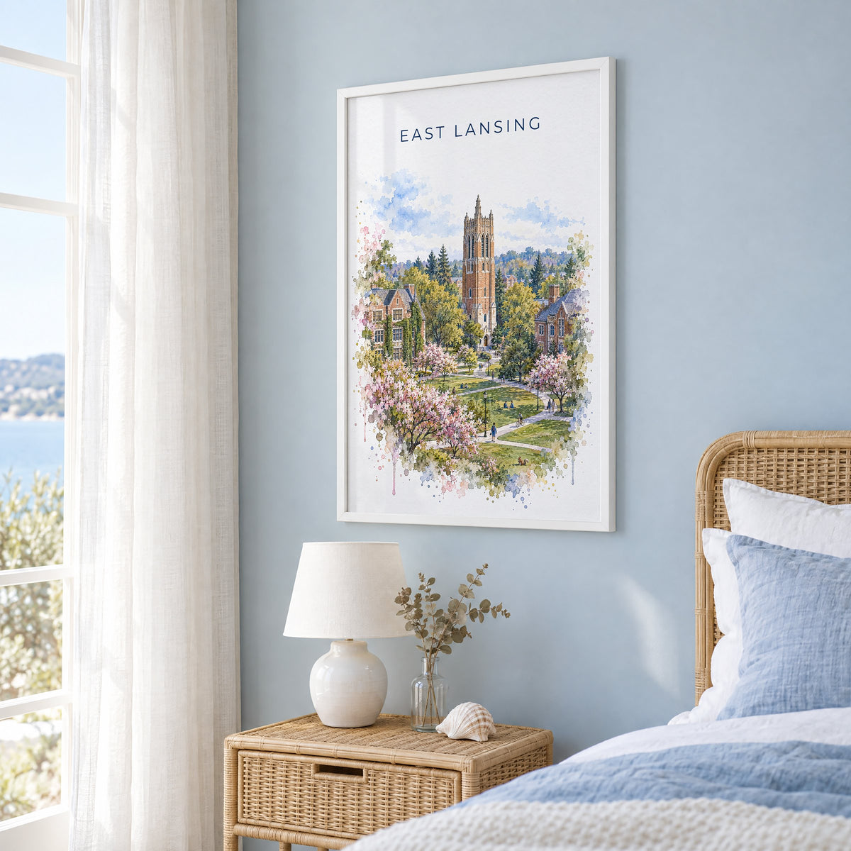 East Lansing watercolor print in a white frame on a pale blue wall beside a rattan bed in a coastal bedroom