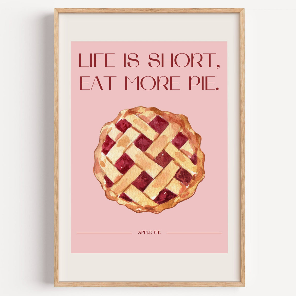 Eat More Pie watercolor print in a light oak frame on a plain white wall