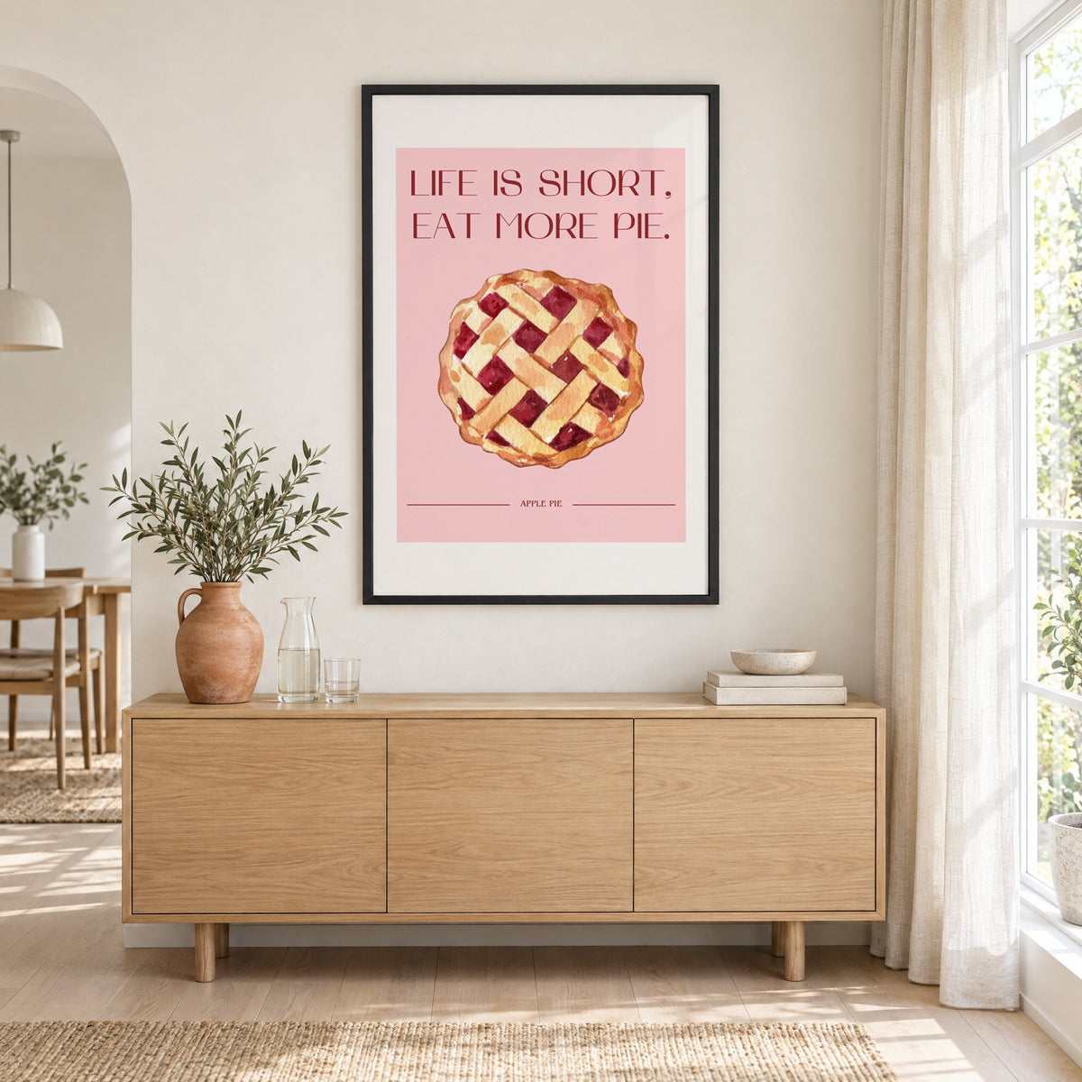 Eat More Pie watercolor print in a black frame above an oak sideboard with a terracotta vase of olive branches
