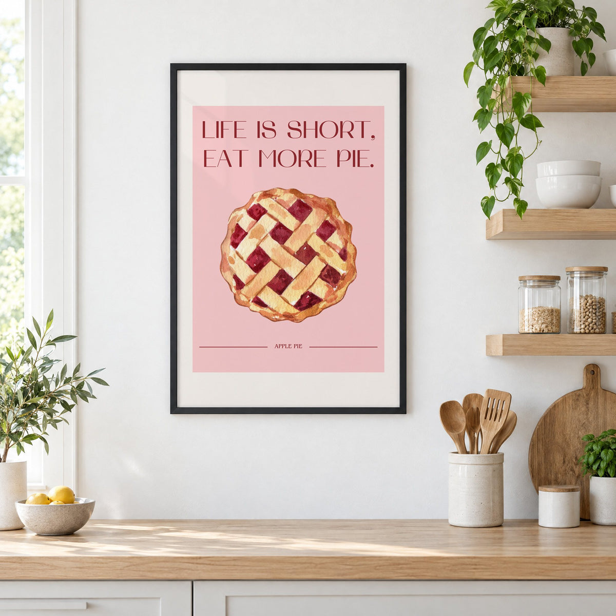 Eat More Pie watercolor print in a black frame in a white kitchen beside open wood shelves and glass jars