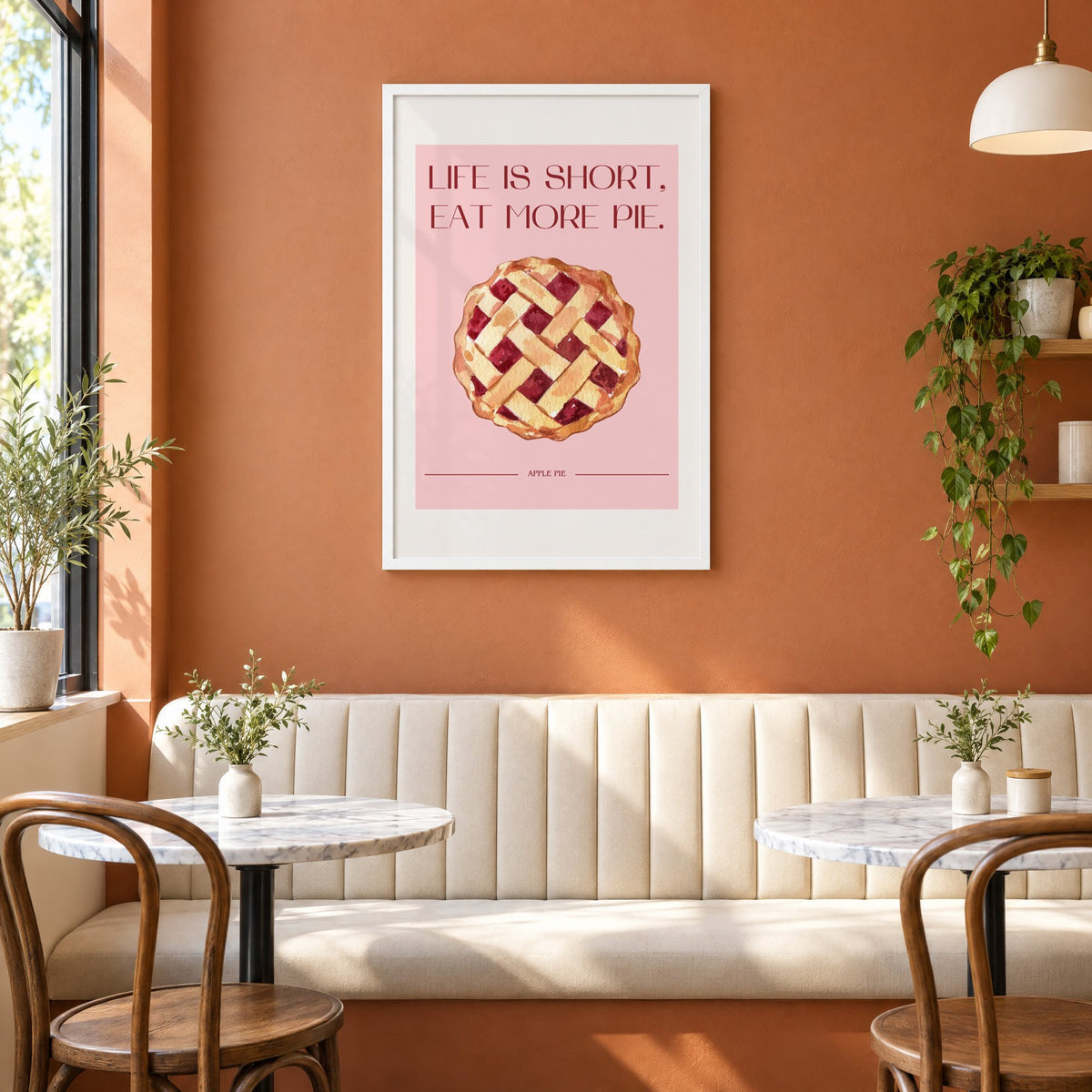 Eat More Pie watercolor print in a white frame above a cream banquette on a terracotta cafe wall