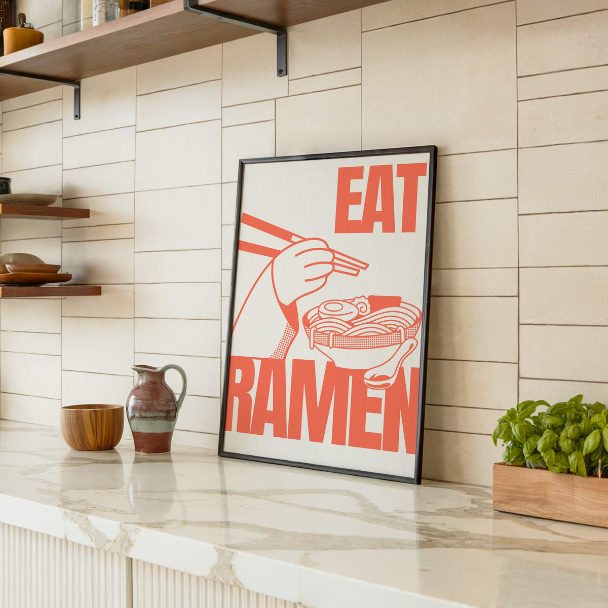 Eat Ramen print in a black frame leaning on a marble counter in a tiled kitchen