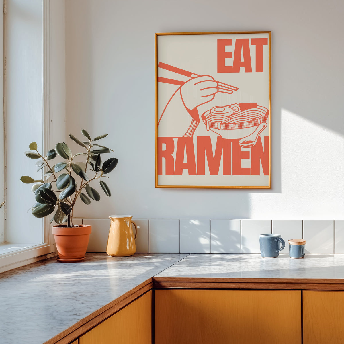 Eat Ramen print shown in a gold frame above a marble counter in a tan kitchen