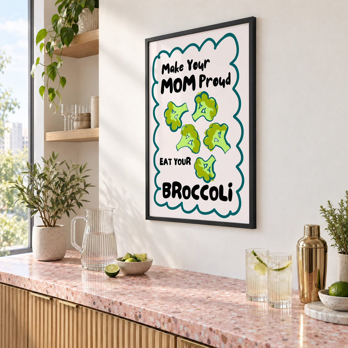 Eat Your Broccoli pink kitchen print in a black frame above a pink terrazzo cocktail counter with limes, seen at an angle