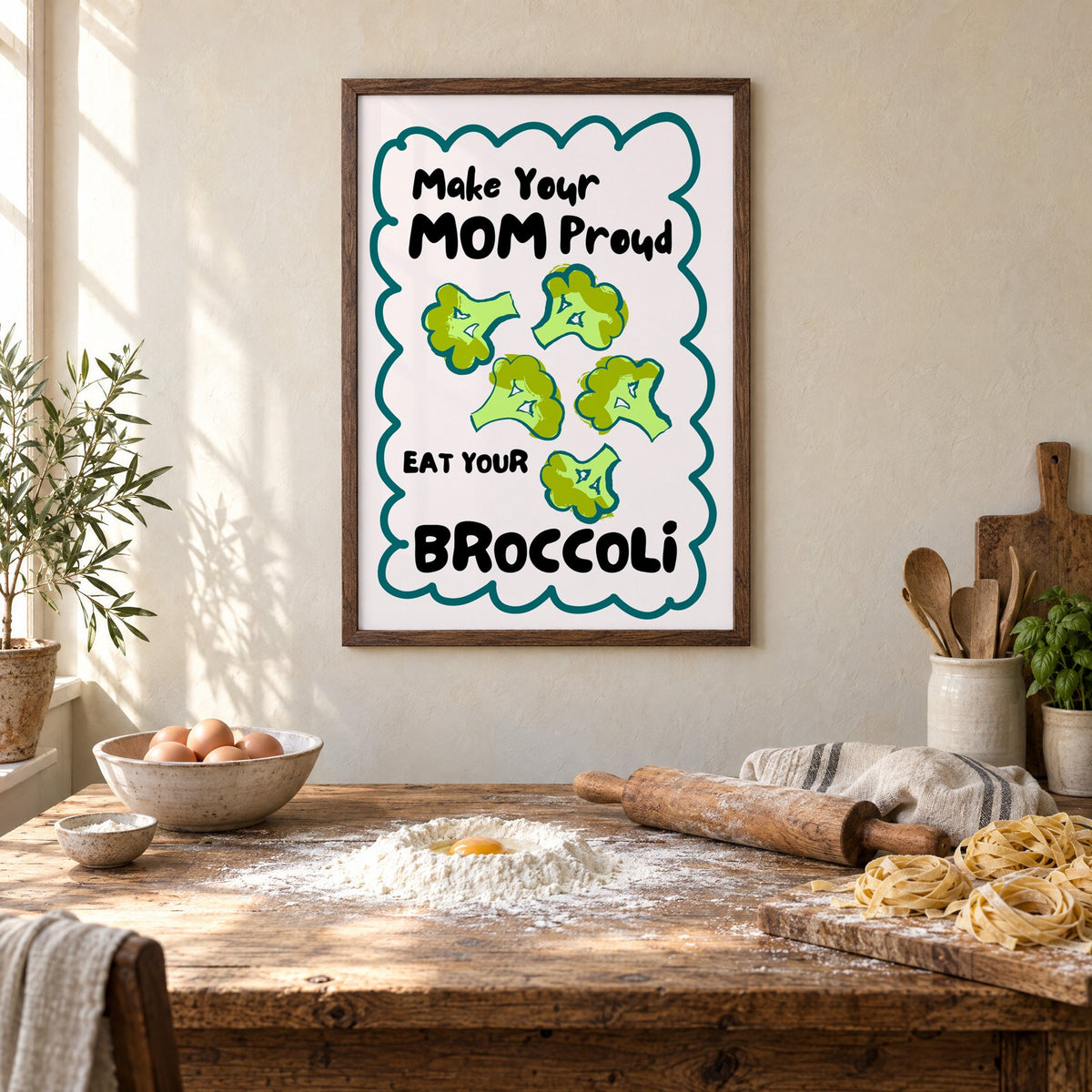 Eat Your Broccoli pink kitchen print in a walnut frame above a rustic table set for making fresh pasta