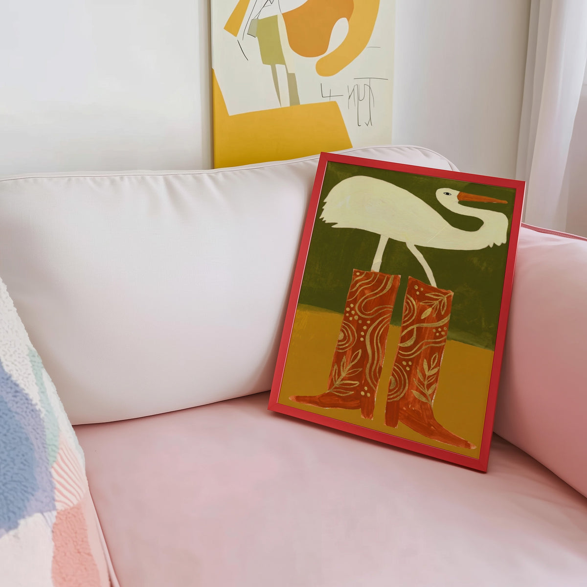 Olive and mustard bird print shown in a red frame leaning on a blush pink sofa