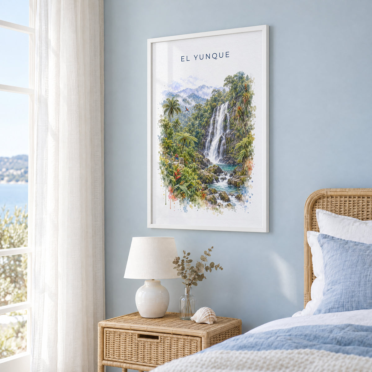El Yunque watercolor print in a white frame on a pale blue wall beside a rattan bed in a coastal bedroom
