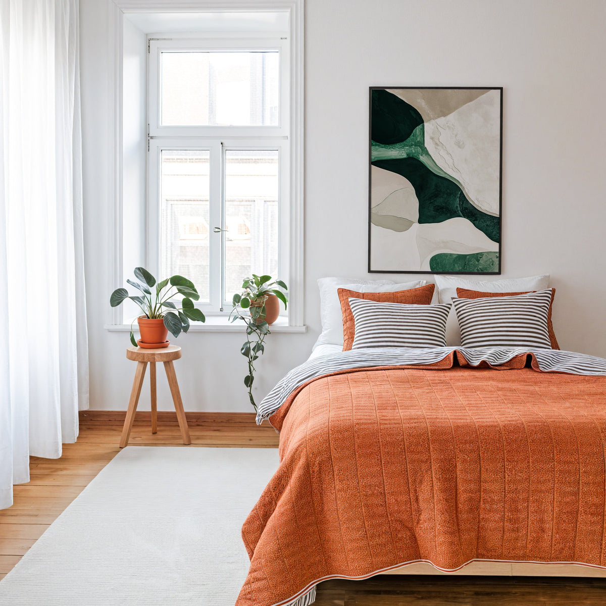 Emerald and cream organic shapes abstract print in a thin black frame above a bed with a rust orange quilt