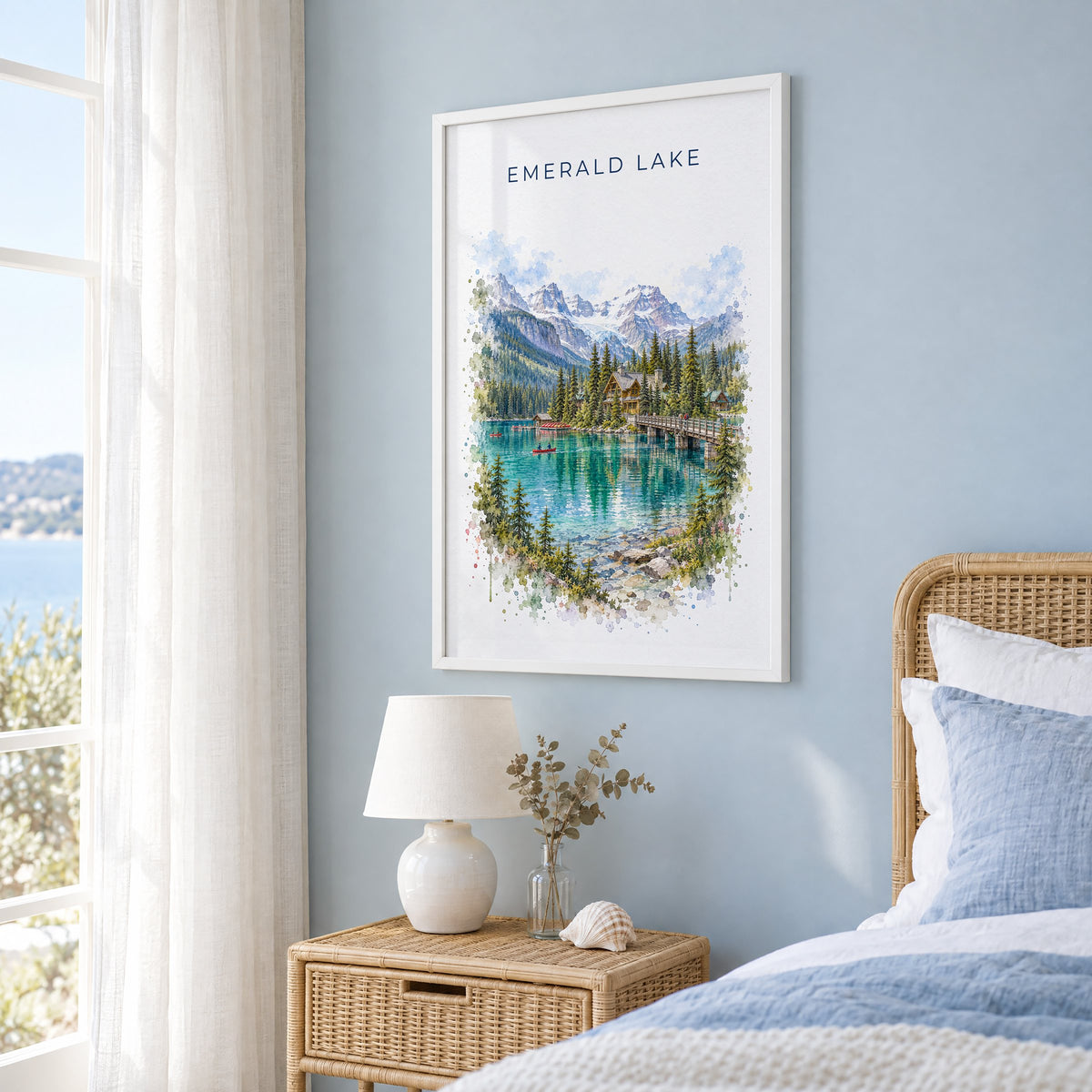 Emerald Lake, BC watercolor print in a white frame on a pale blue wall beside a rattan bed in a coastal bedroom