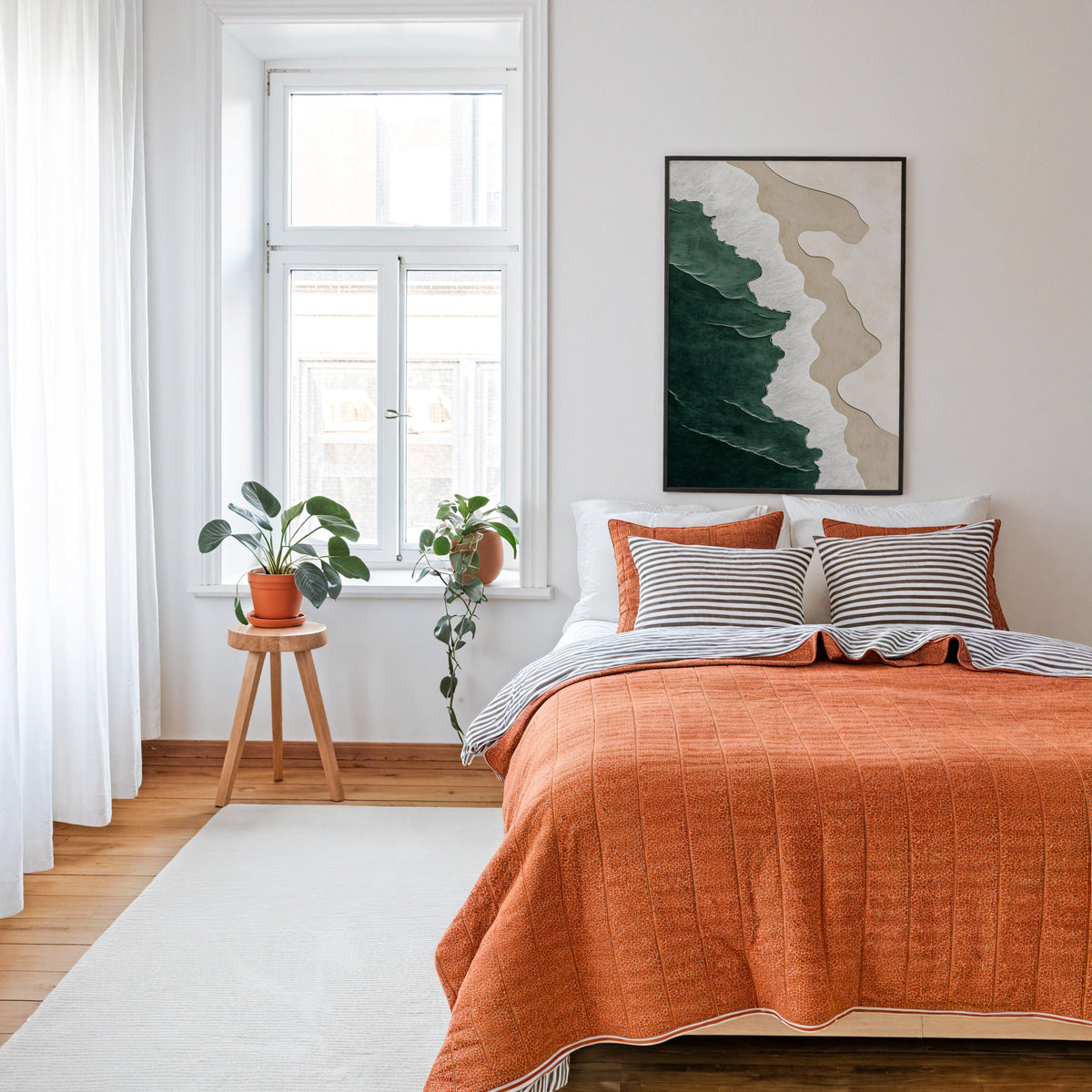 Emerald, white and sand shoreline abstract print in a thin black frame above a bed with a rust orange quilt