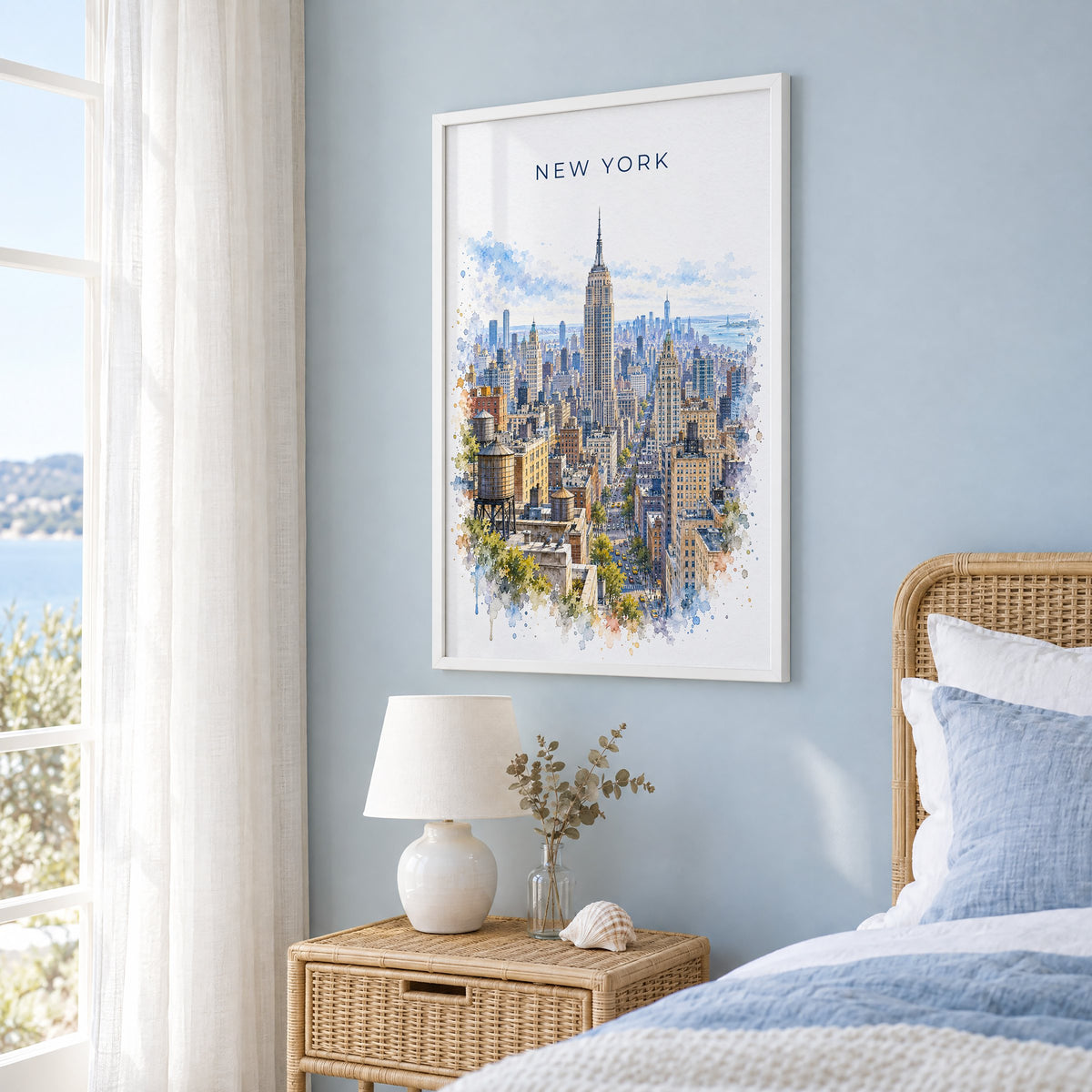 Empire State Building watercolor print in a white frame on a pale blue wall beside a rattan bed in a coastal bedroom
