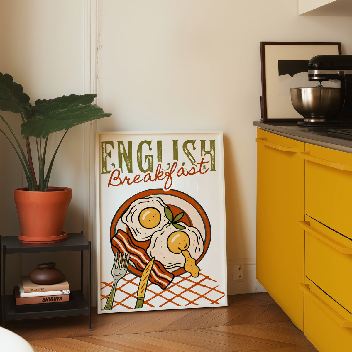 English breakfast print in a white frame leaning on parquet beside a yellow kitchen