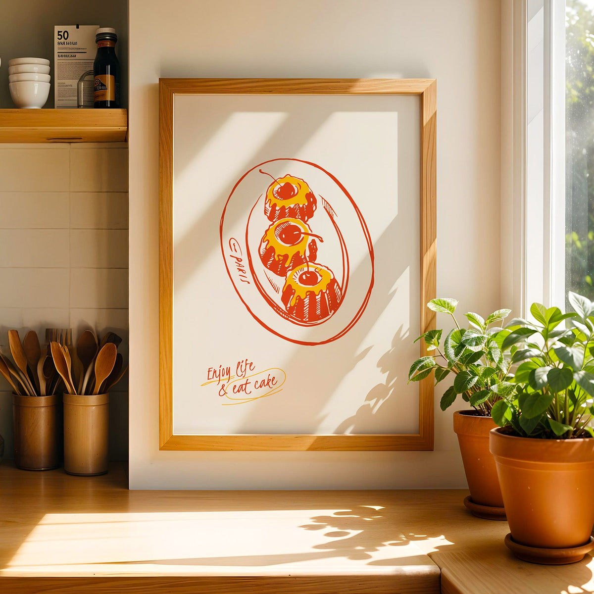 Enjoy Life and Eat Cake print in a light pine frame beside a jar of wooden spoons