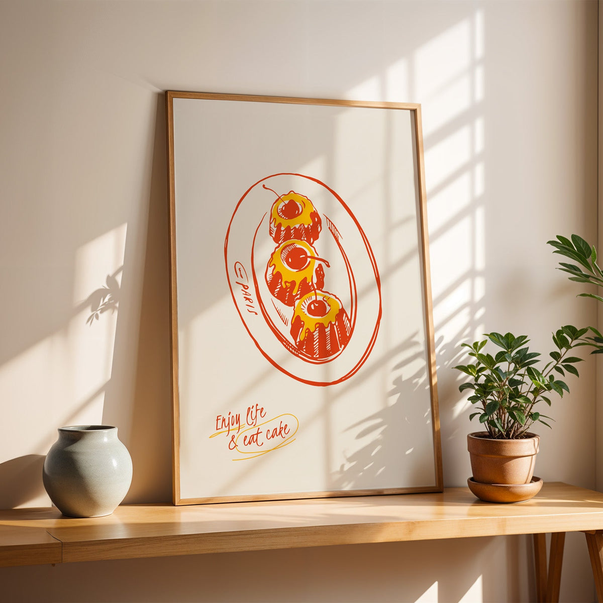 Enjoy Life and Eat Cake print in a slim oak frame on a console with a grey-blue vase